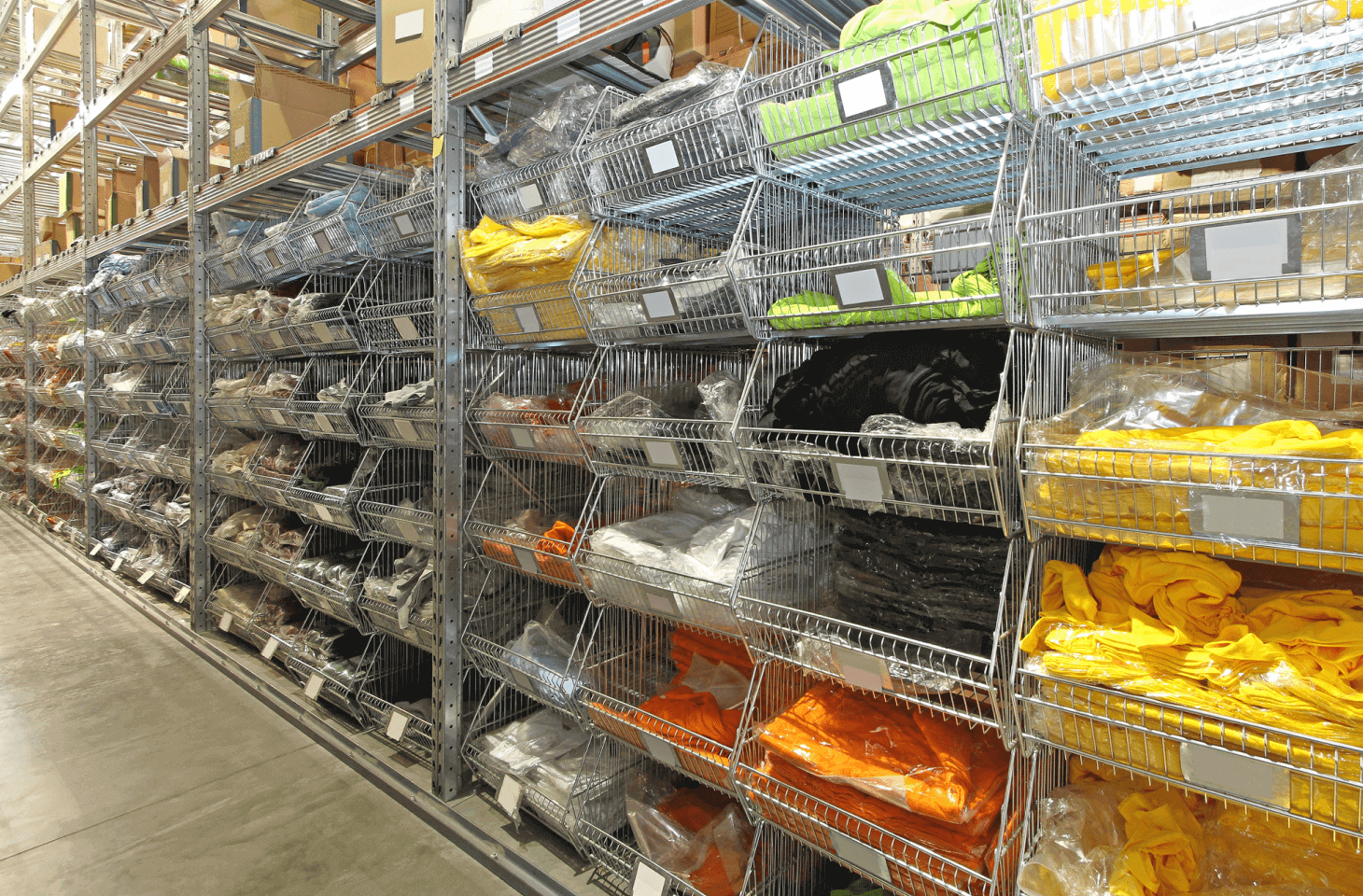 Warehouse interior with metal shelves holding various folded clothing items sorted by color, including yellow, orange, and black.